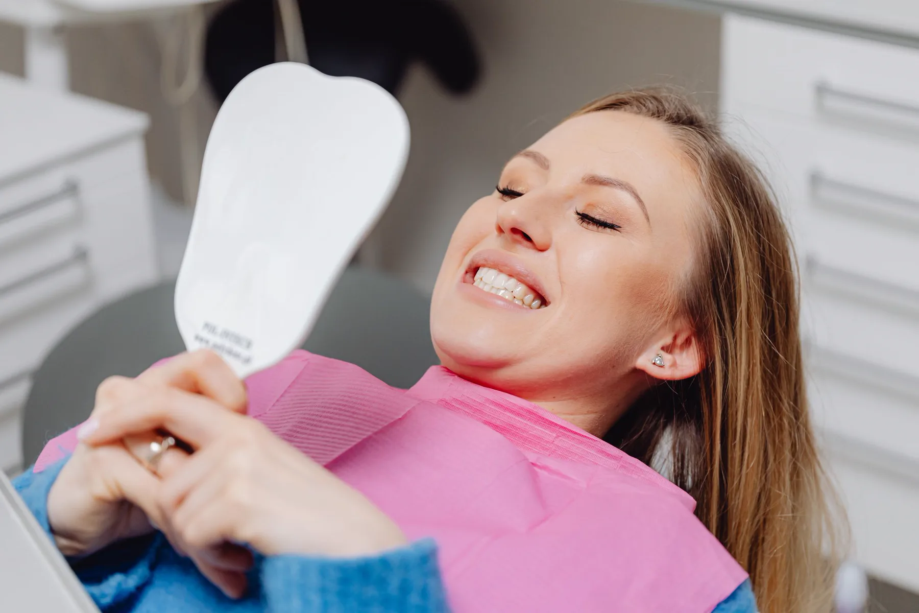 A patient smiling as she sees her result in the mirror